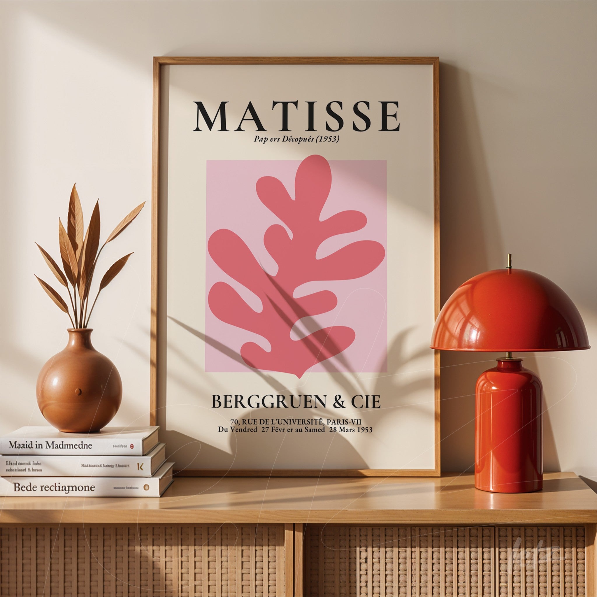 quadro decorativo estilo moderno com fundo rosa e formas abstractas em moldura clara, apoiado em prateleira de madeira ao lado de vaso de cerâmica e abajur vermelho