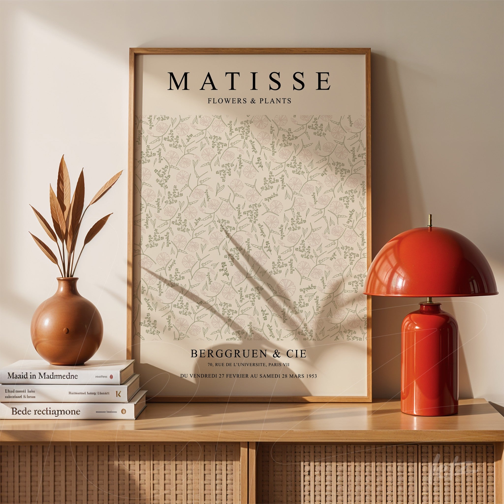 quadro com arte de plantas de matisse em moldura de madeira clara apoiado sobre uma mesa com vaso e luminária vermelha