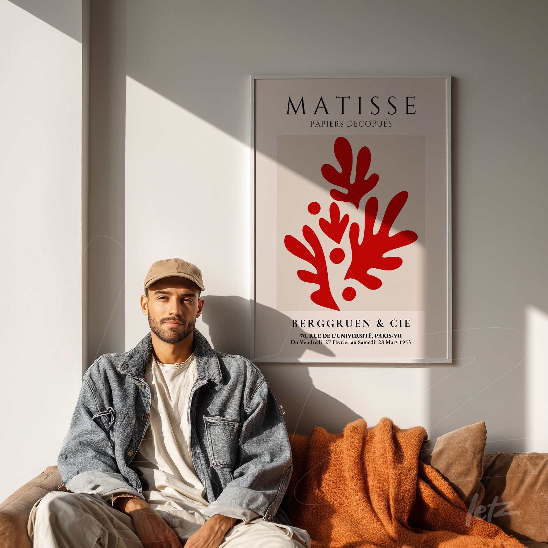 quadro em moldura branca com a arte de Matisse apresentando formas orgânicas em vermelho, apoiado na parede ao lado de um homem com boné e jaqueta azul