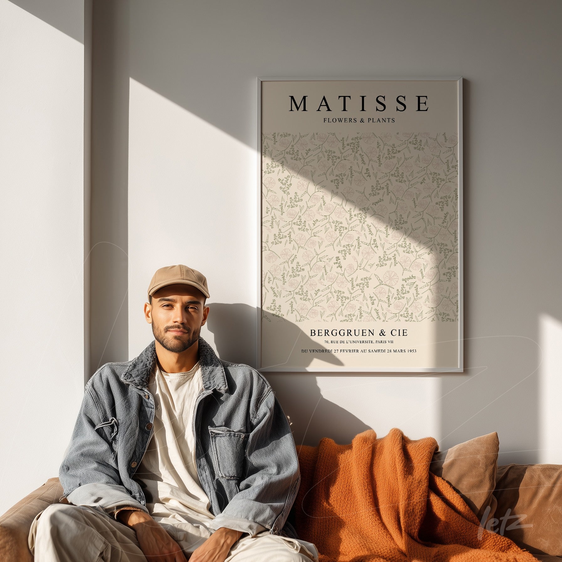 quadro com arte floral de Matisse em moldura branca, exposto ao lado de um homem sentado em sofá marrom