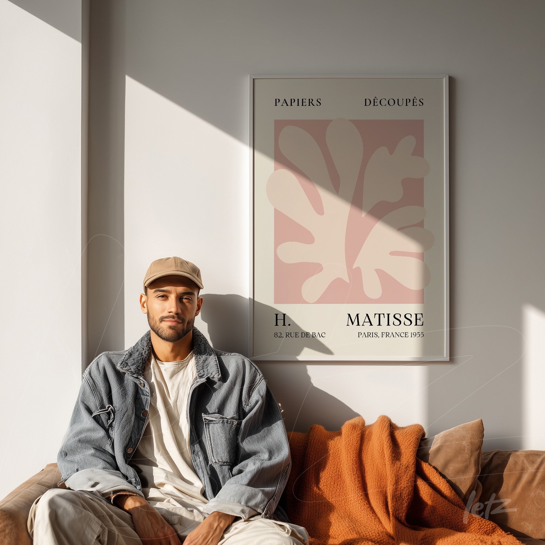 quadro decorativo com arte de Henri Matisse em moldura branca, exibido sobre parede clara, com sofá marrom e manta laranja ao fundo