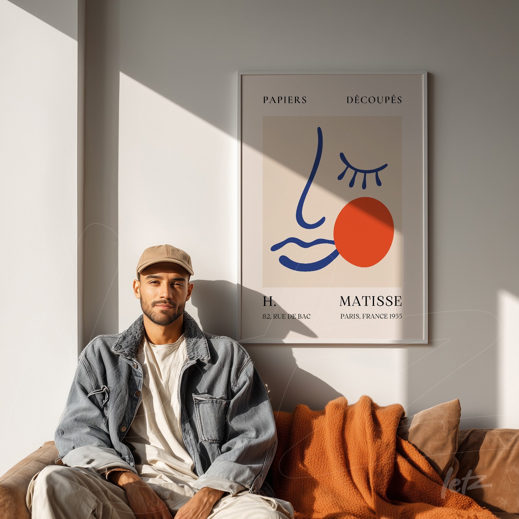 quadro decorativo com arte abstrata de rosto feminino em moldura clara, ao lado de homem sentado em sofá com cobertor laranja