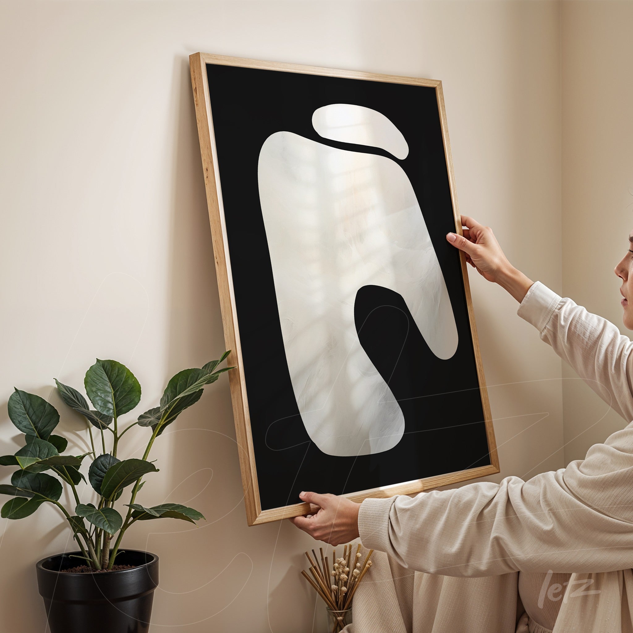 quadro com arte abstrata de formatos fluidos em moldura de madeira clara sobre parede bege