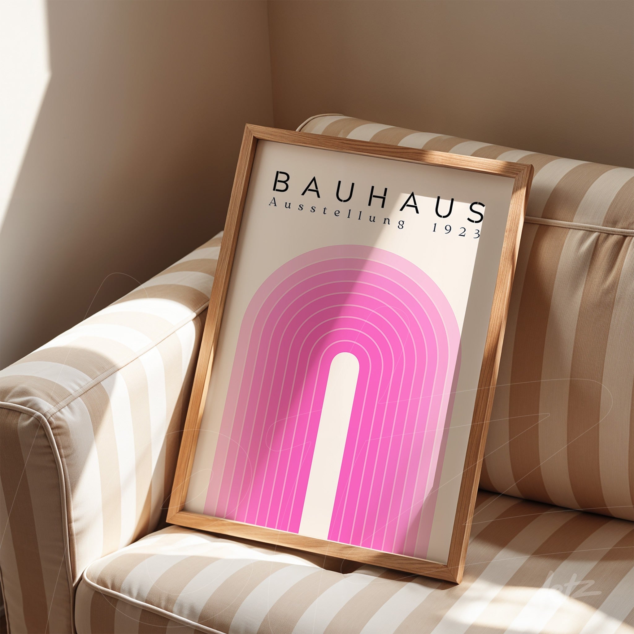 quadro apoiado em sofá listrado com arte minimalista do movimento Bauhaus em tons de rosa e moldura de madeira clara