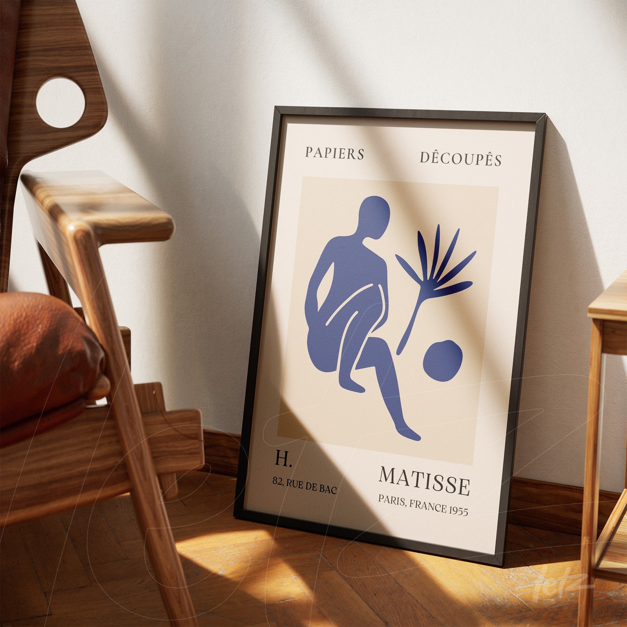 quadro decorativo com arte moderna de figura humana e planta em moldura preta, apoiado em parede clara ao lado de cadeira de madeira