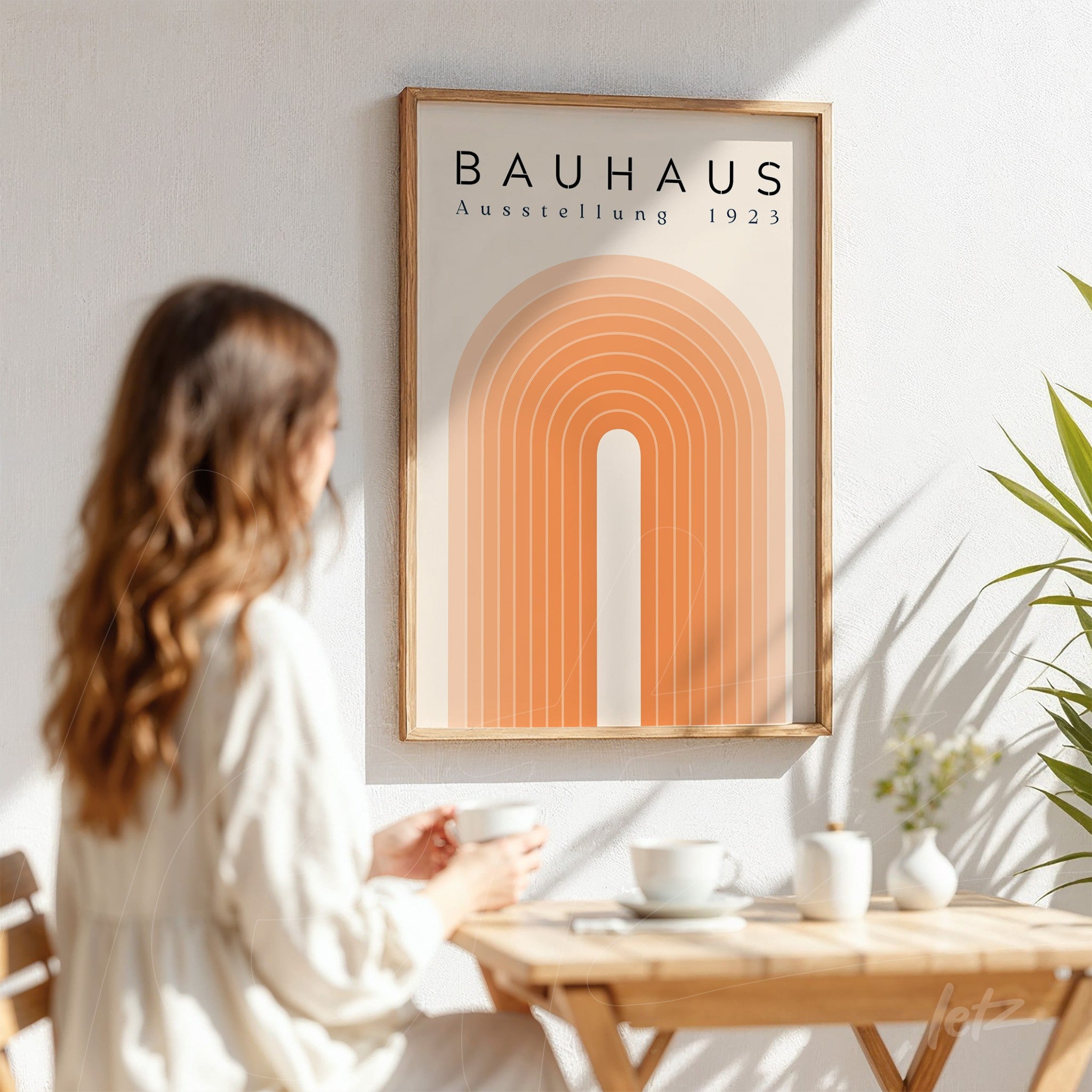 quadro com arte geométrica estilo bauhaus de arcos laranja exibido em moldura de madeira clara sobre parede branca ao lado de uma pessoa tomando café