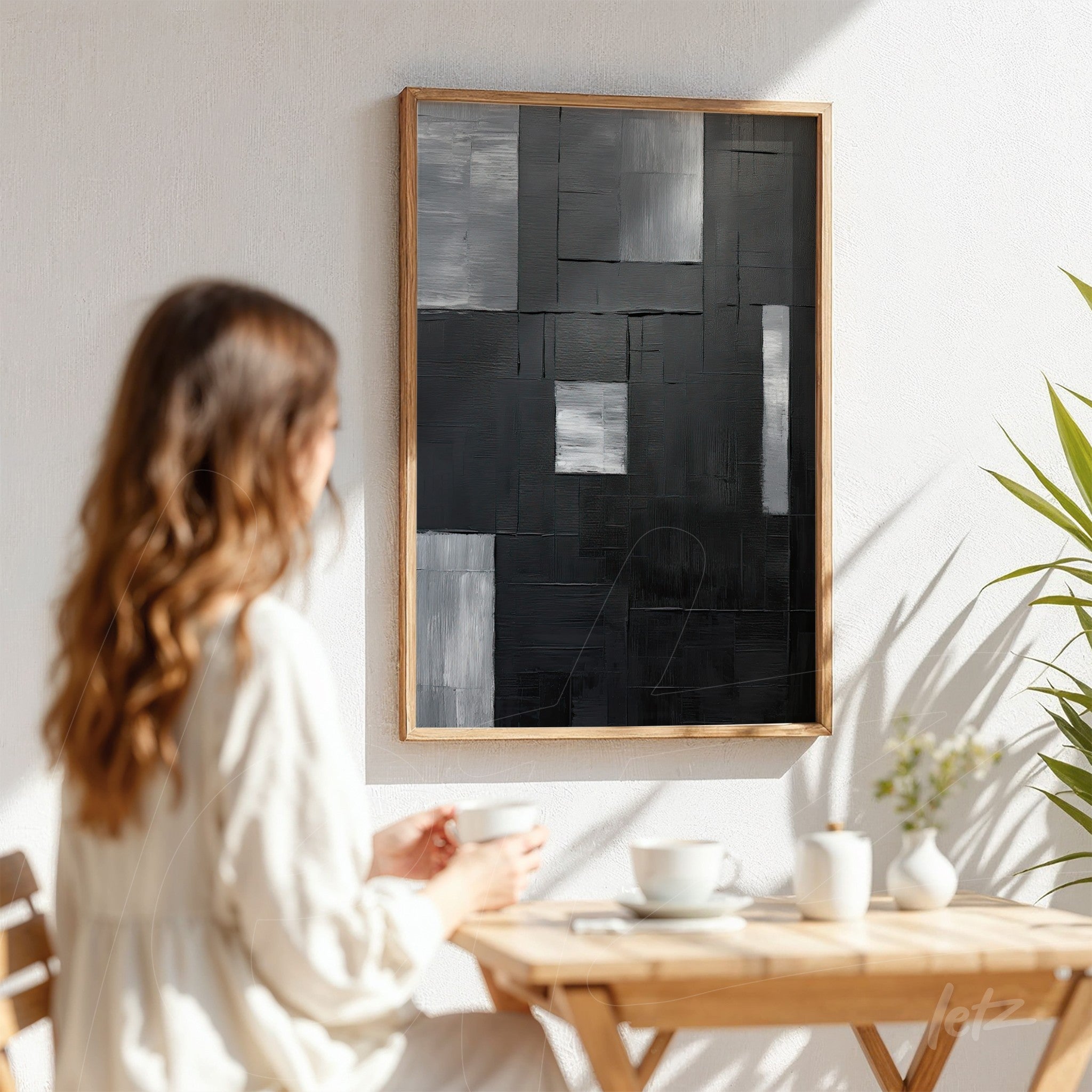 quadro abstrato em tons de preto e cinza com acabamento em moldura de madeira clara, exibido sobre parede branca