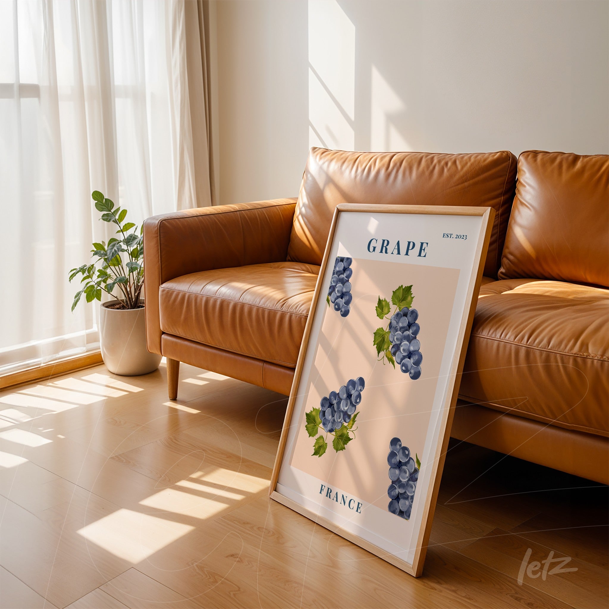 quadro decorativo de uvas roxas em fundo rosa claro com moldura de madeira clara, apoiado ao lado de um sofá de couro caramelizado