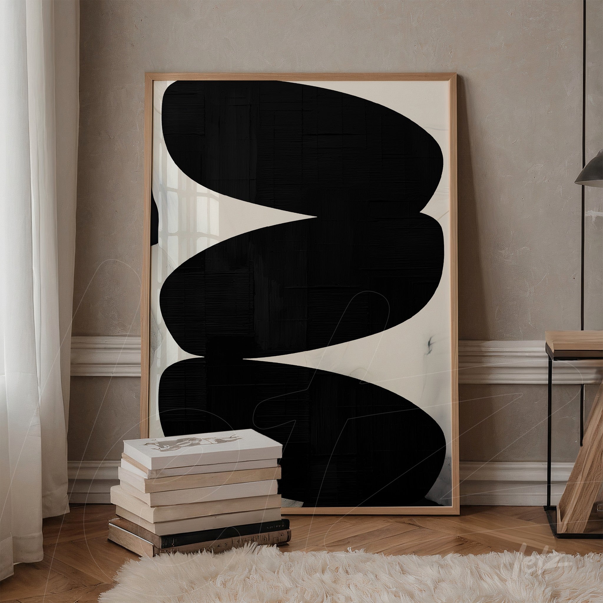 quadro com arte abstrata em preto e branco em moldura clara, apoiado em pilha de livros sobre mesa ao lado de uma parede com textura clara