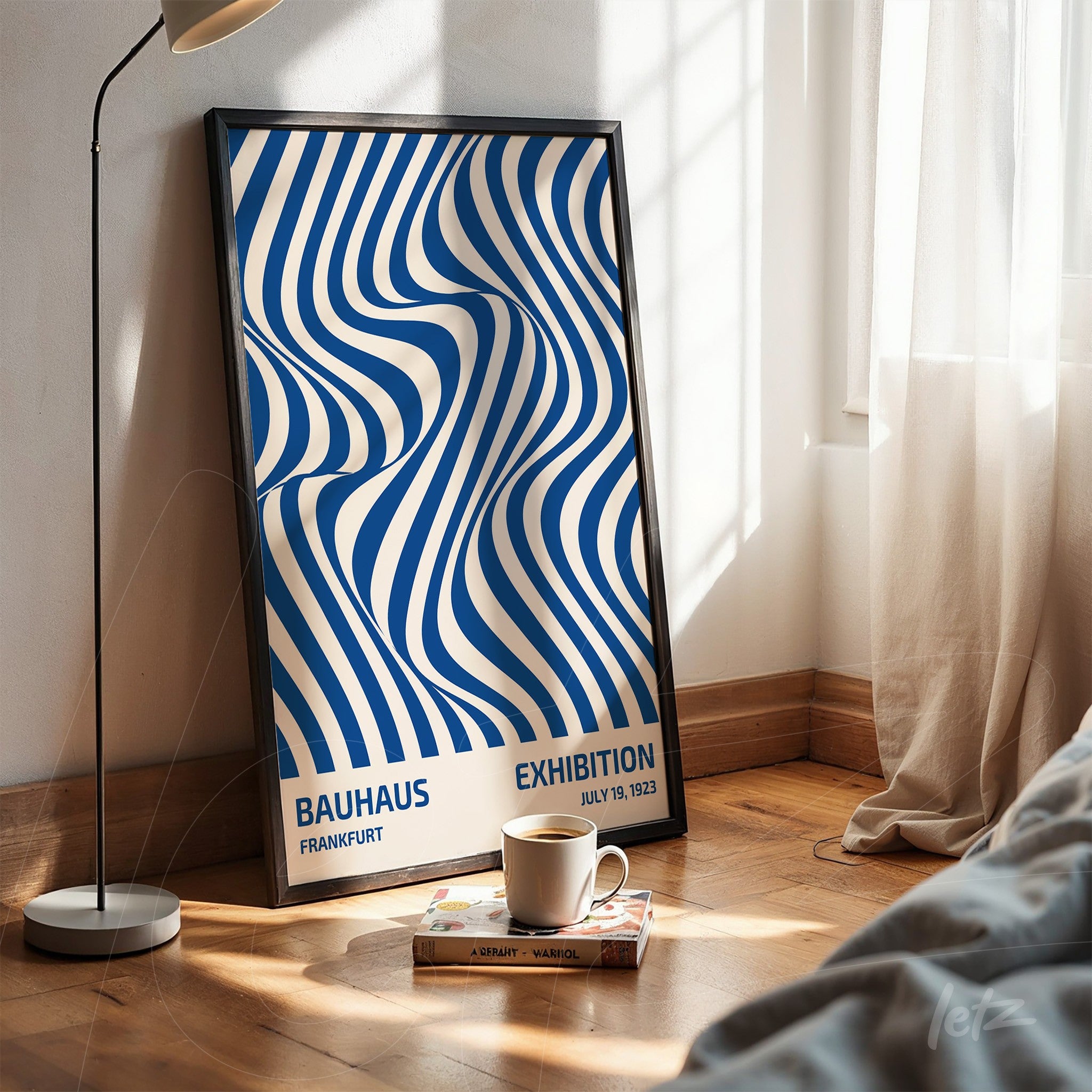 pôster com ilustração geométrica em azul e branco com moldura preta apoiada no chão em ambiente iluminado por janela