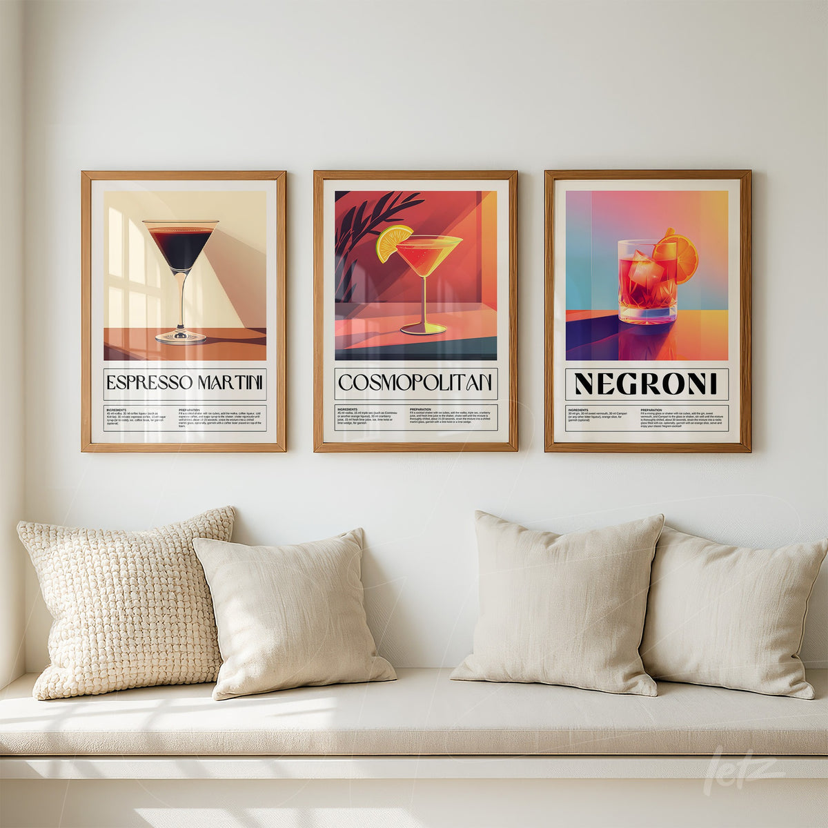 composição de três quadros decorativos com coquetéis coloridos em moldura de madeira clara, incluindo espresso martini, cosmopolitan e negroni, dispostos sobre uma parede clara ao lado de almofadas bege