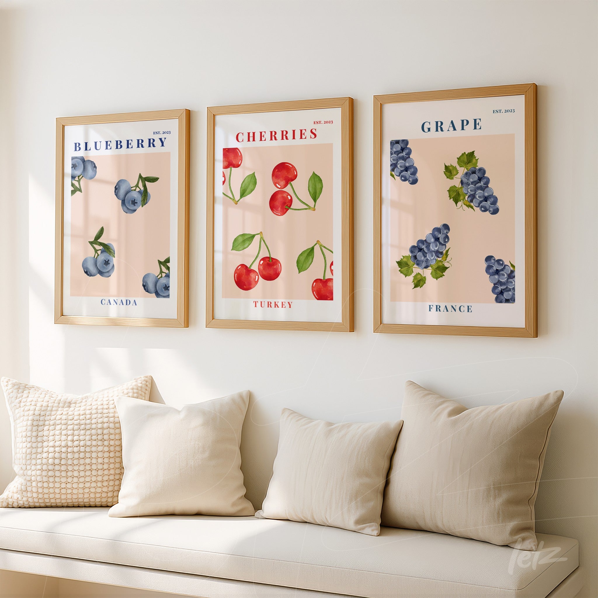 composição de quadros decorativos com frutas: mirtilos, cerejas e uvas em moldura de madeira clara, expostos em uma parede com fundo neutro e almofadas claras à frente