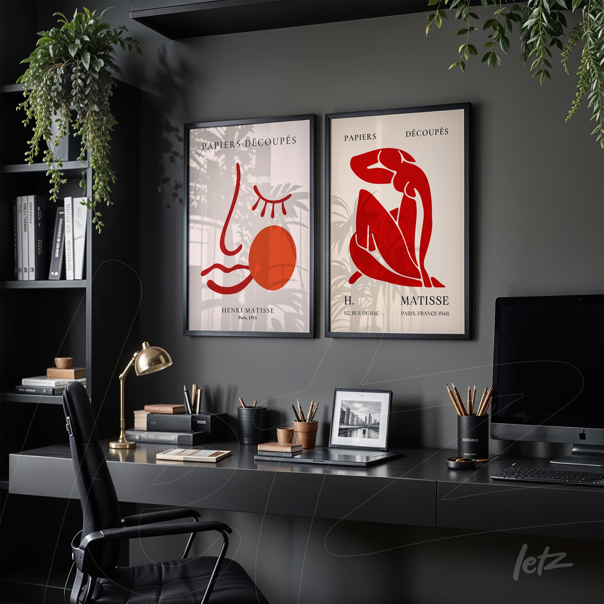 composição com dois quadros decorativos em moldura preta, um com uma linha abstrata de rosto e círculo vermelho, e o outro retratando uma figura feminina em estilo minimalista, ambos sobre parede escura em ambiente de escritório