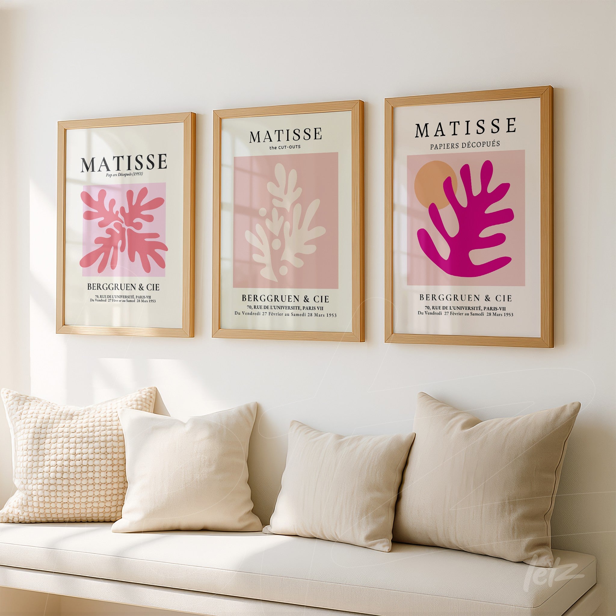 composição de três quadros em moldura bege com arte abstrata em tons de rosa e vermelho, exibidos sobre parede clara, com almofadas neutras em sofá de tecido