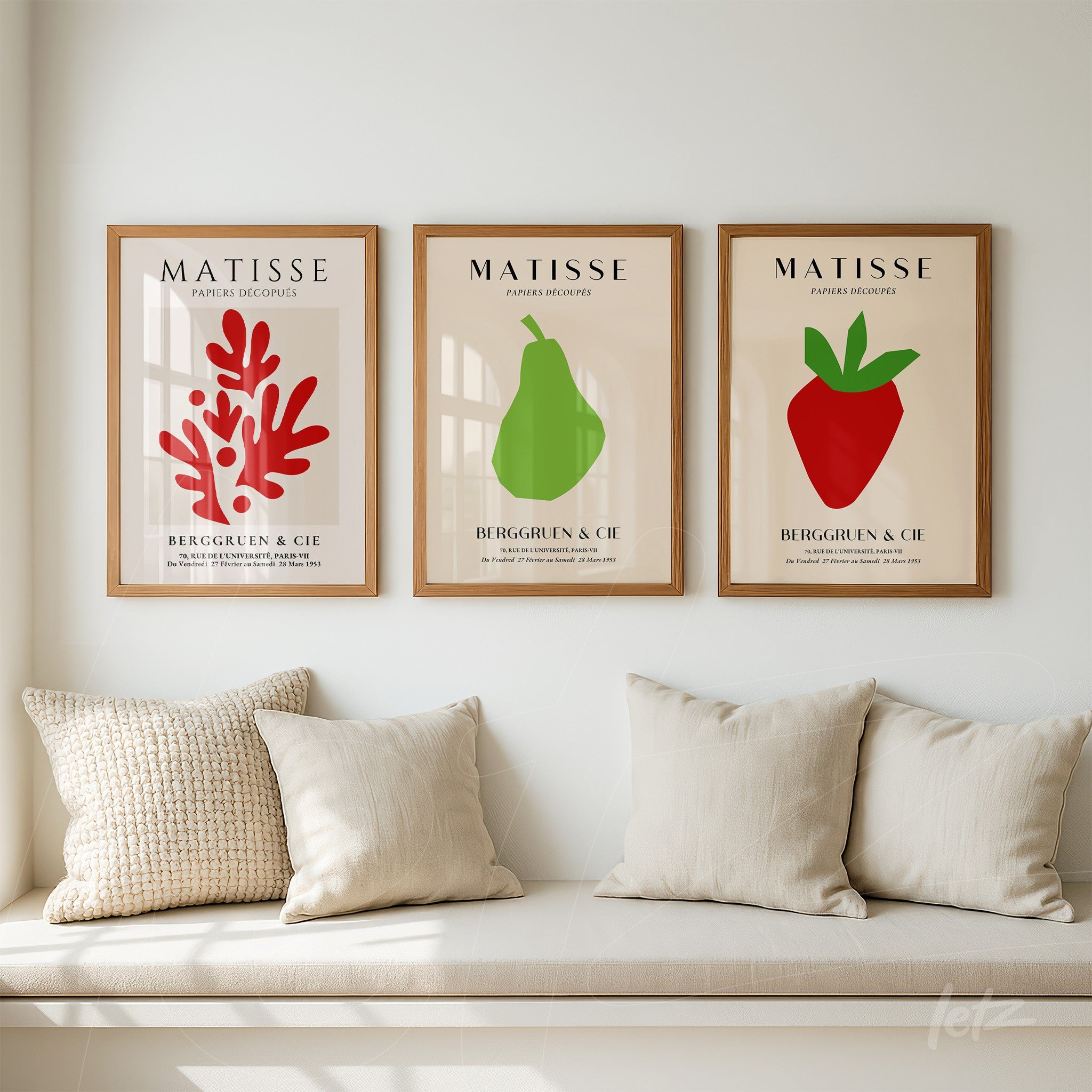 composição de três quadros com arte simples de frutas e vegetação em molduras de madeira clara, exibidos sobre sofá neutro