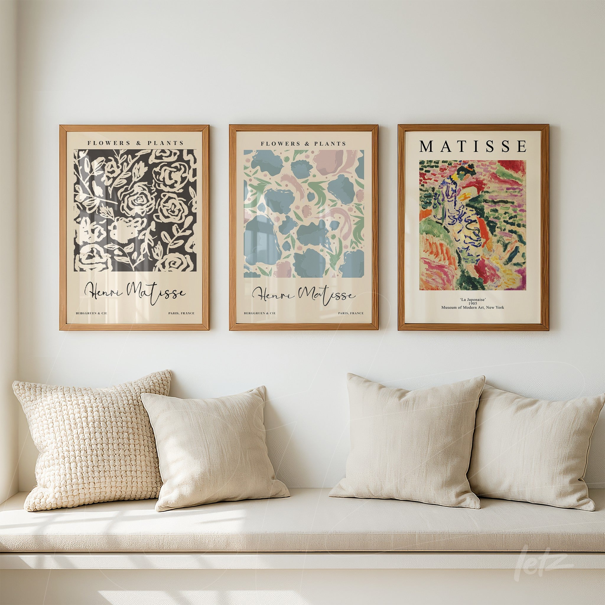 composição com três quadros decorativos de arte moderna em moldura de madeira clara, exibidos sobre um sofá com almofadas claras
