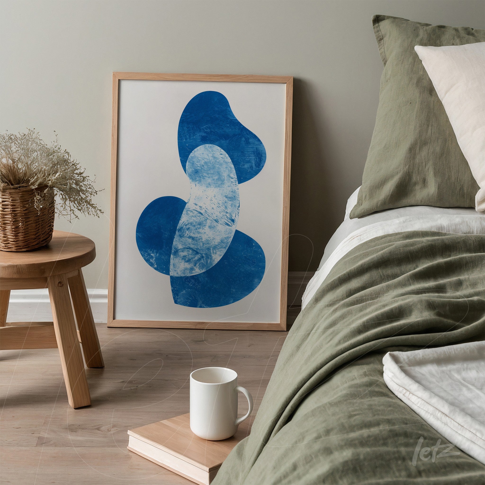 quadro com arte abstrata em azul emoldurado com moldura clara sobre mesa ao lado de cama