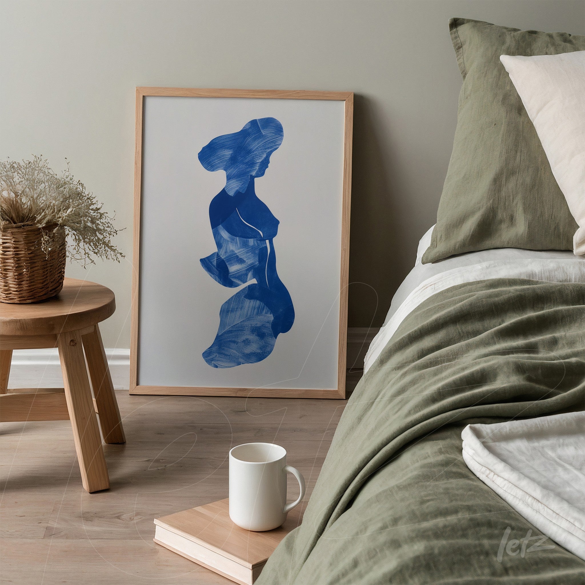 quadro com arte em azul de silhueta feminina em moldura de madeira clara, exibido ao lado de cama com roupas de cama em tons neutros