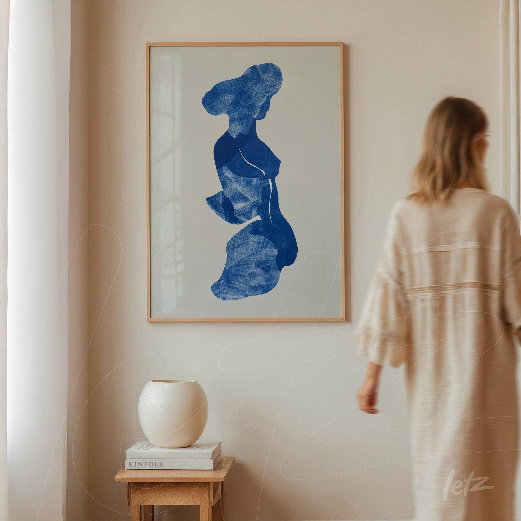 quadro com ilustração abstrata em azul de silhueta feminina em moldura clara sobre parede neutra