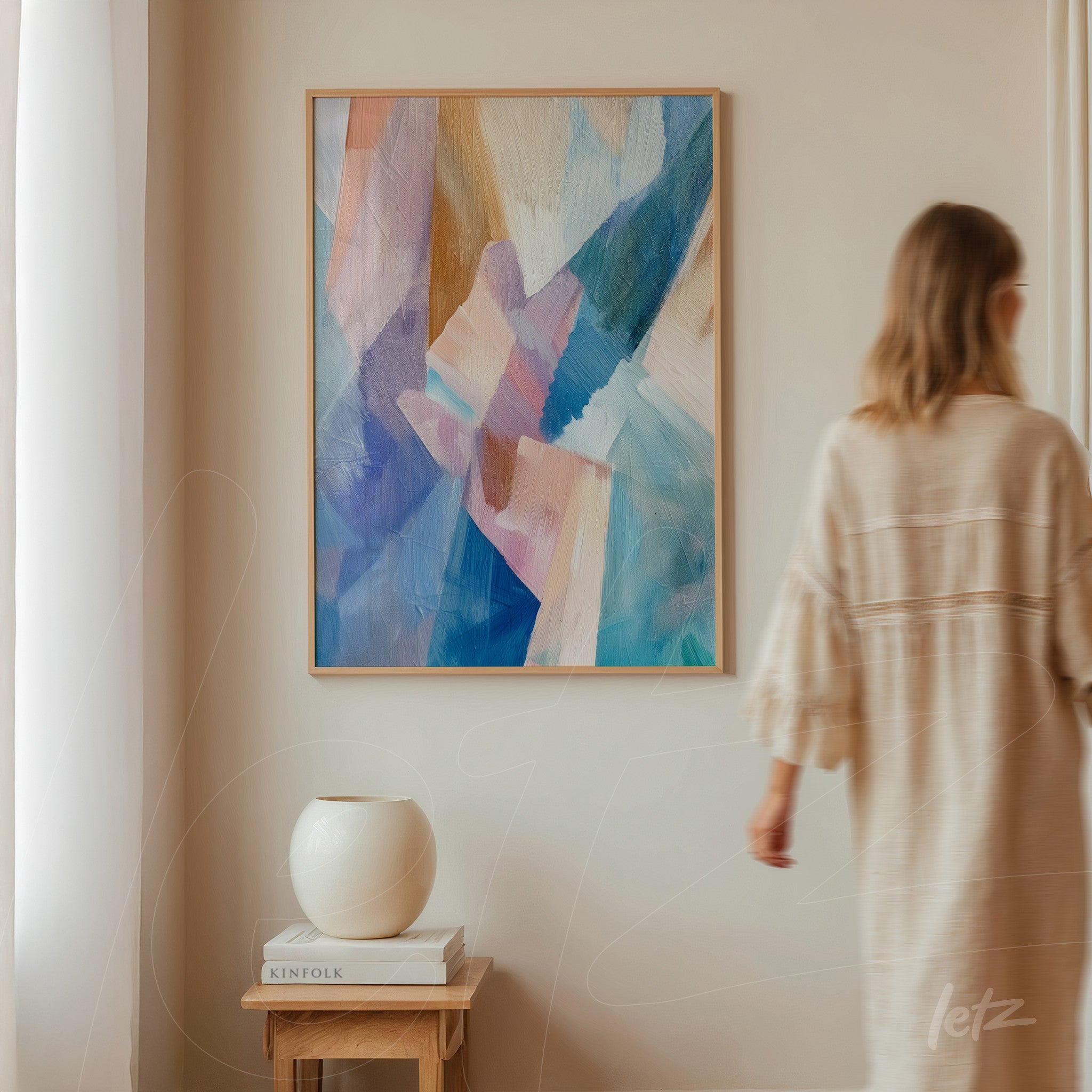 quadro abstrato com pinceladas em tons de azul e rosa em moldura clara, exibido em uma parede neutra