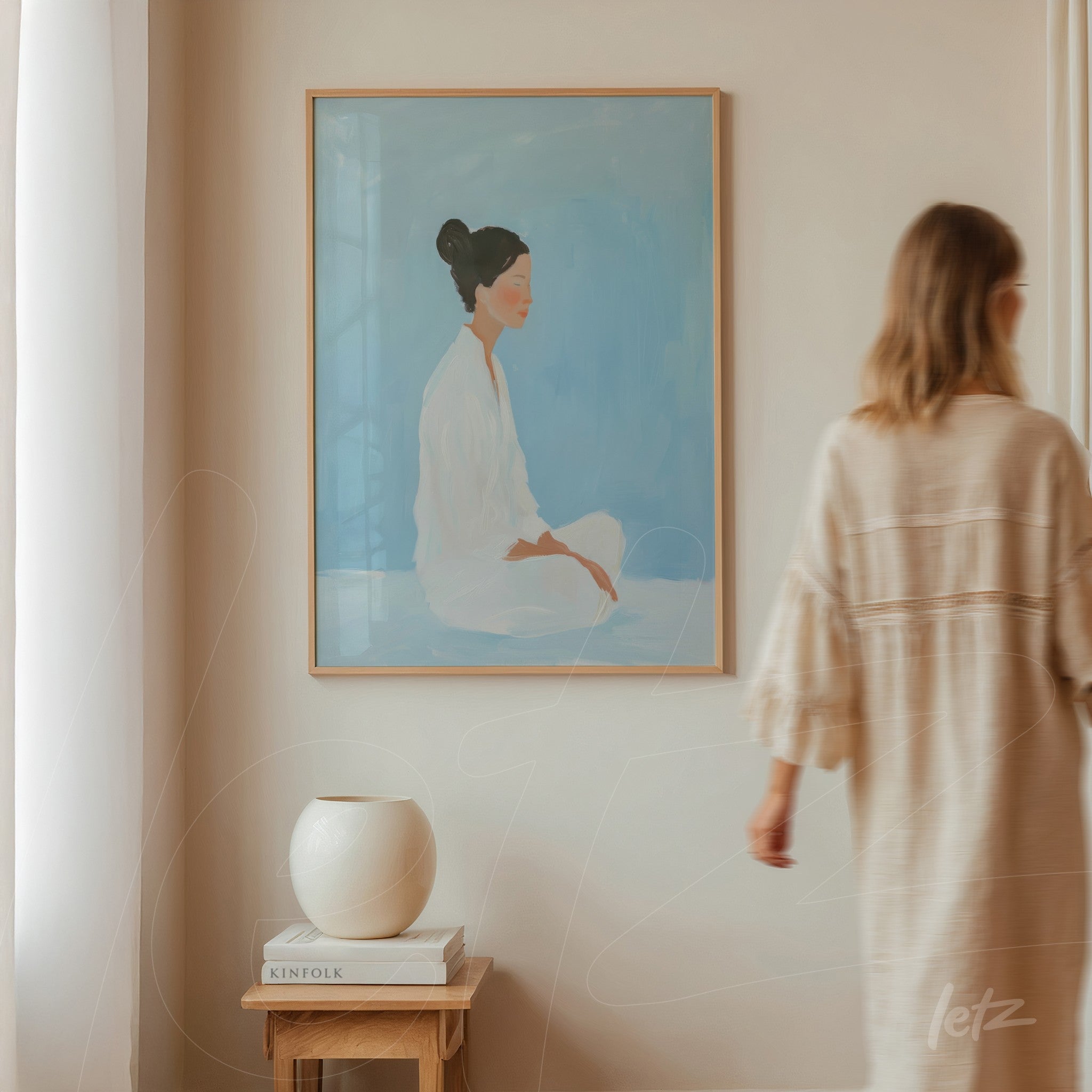 quadro com arte minimalista retratando uma mulher sentada em fundo azul claro, moldura em madeira clara, exposto em ambiente com parede neutra