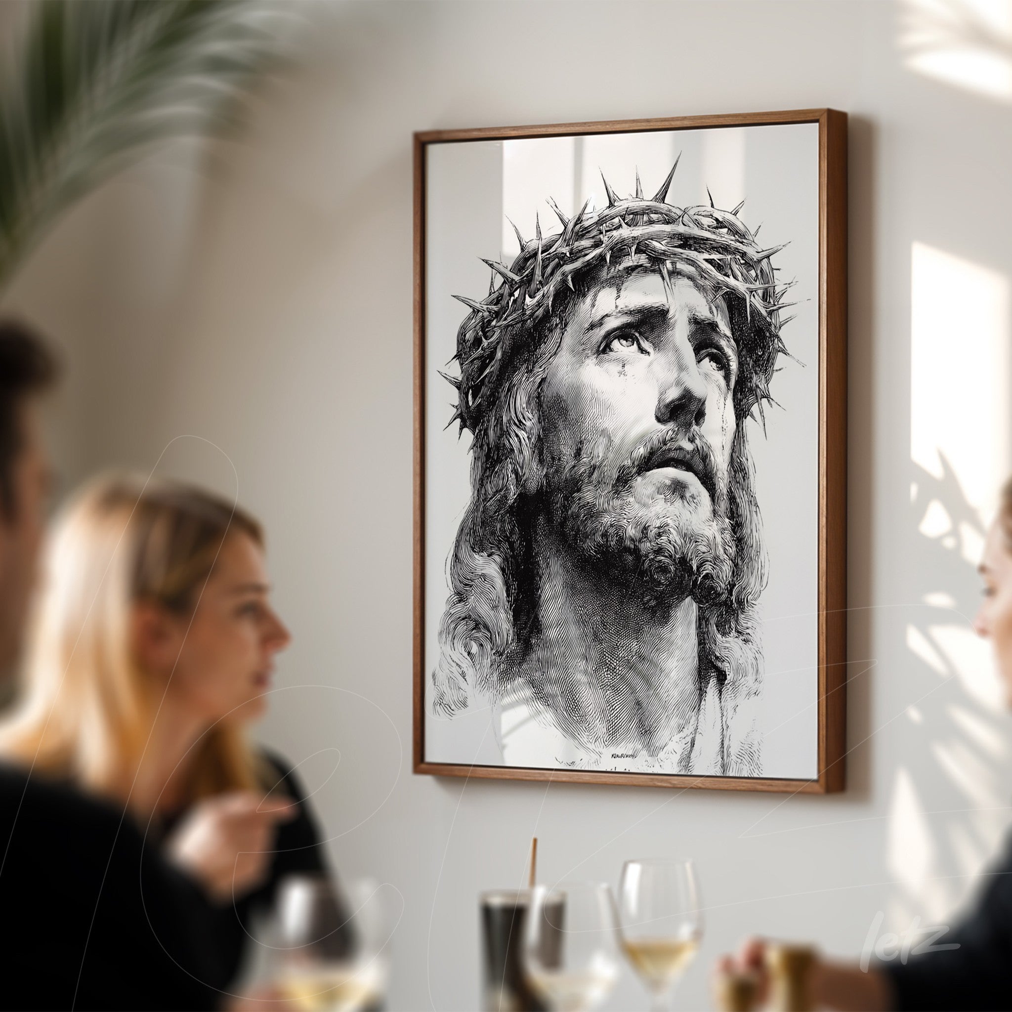 quadro emoldurado retratando a face de Cristo com coroa de espinhos, exibido em parede clara, com pessoas ao fundo em um ambiente de confraternização