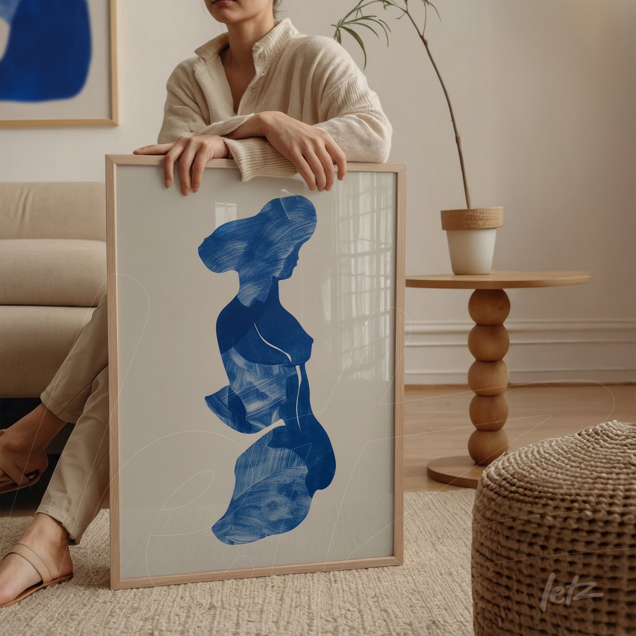 quadro com arte de silhueta feminina em azul, moldura de madeira clara, apoiado em superfície de mesa redonda