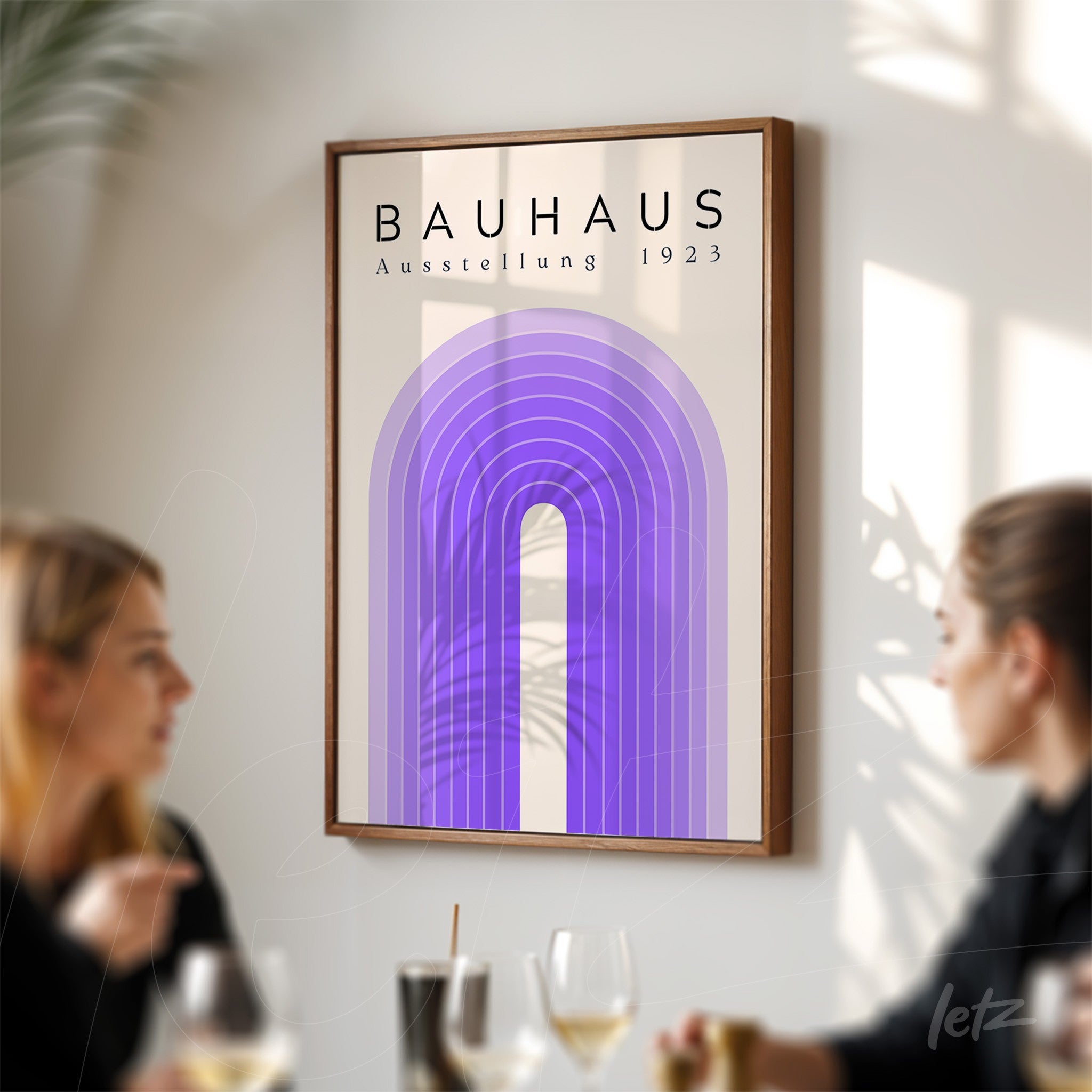 impressão em pôster com design geométrico em tons de roxo e texto 'bauhaus ausstellung 1923', emoldurado em madeira e exibido em uma parede ao lado de mesa com pessoas