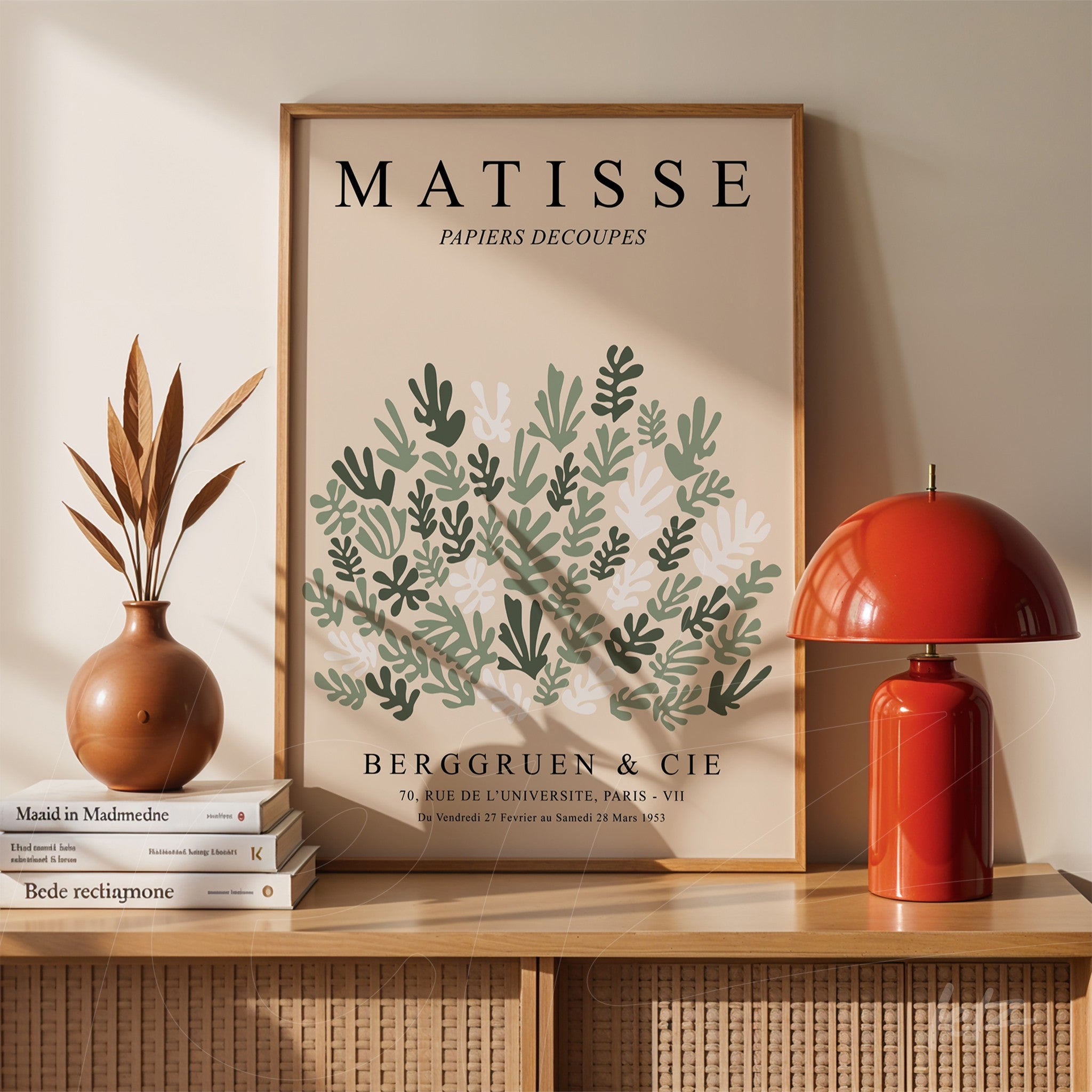 quadro com arte de folhagem em estilo moderno exibido sobre mesa de madeira, ao lado de abajur vermelho e vaso com plantas secas