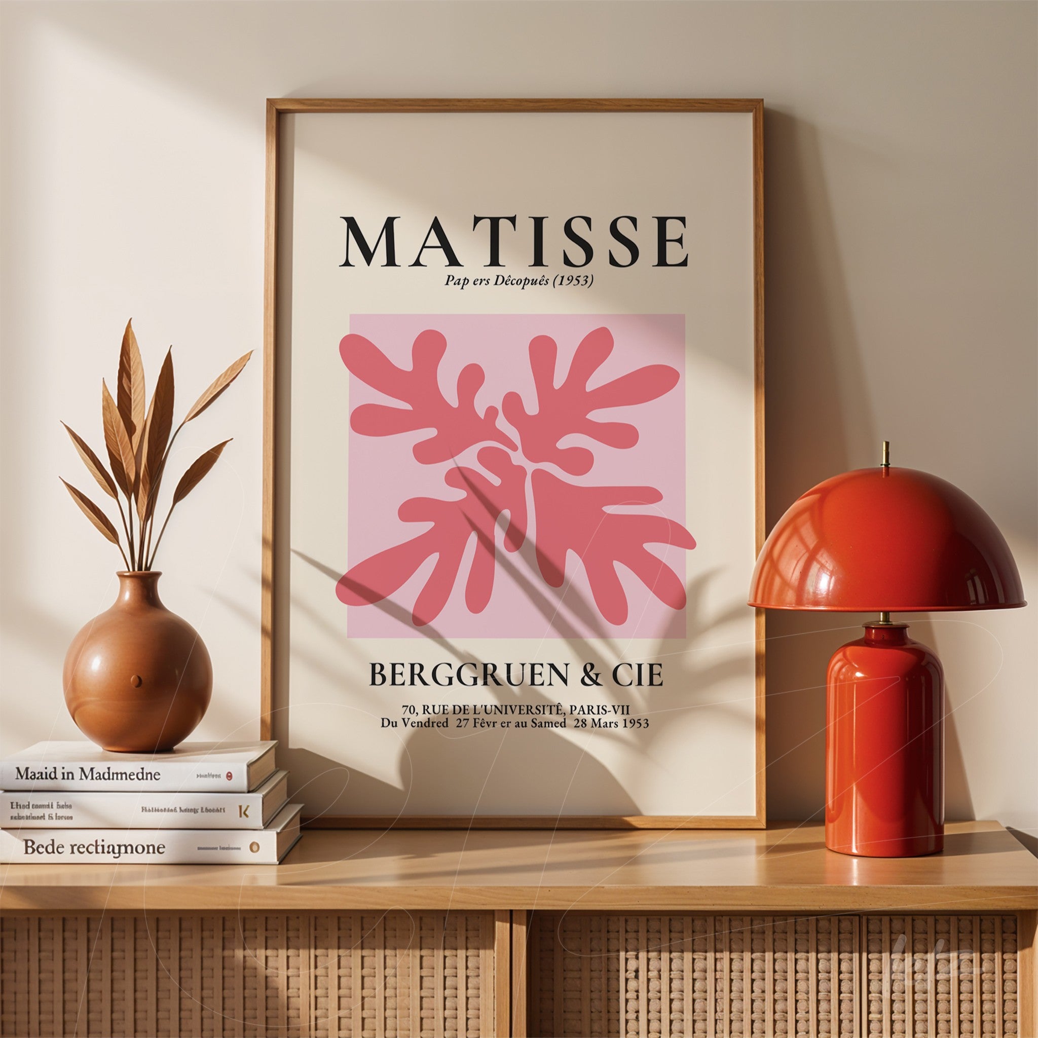 quadro decorativo com arte moderna em tons de rosa e vermelho de planta tropical, moldura branca, exibido em ambiente com prateleira de madeira e luminária vermelha