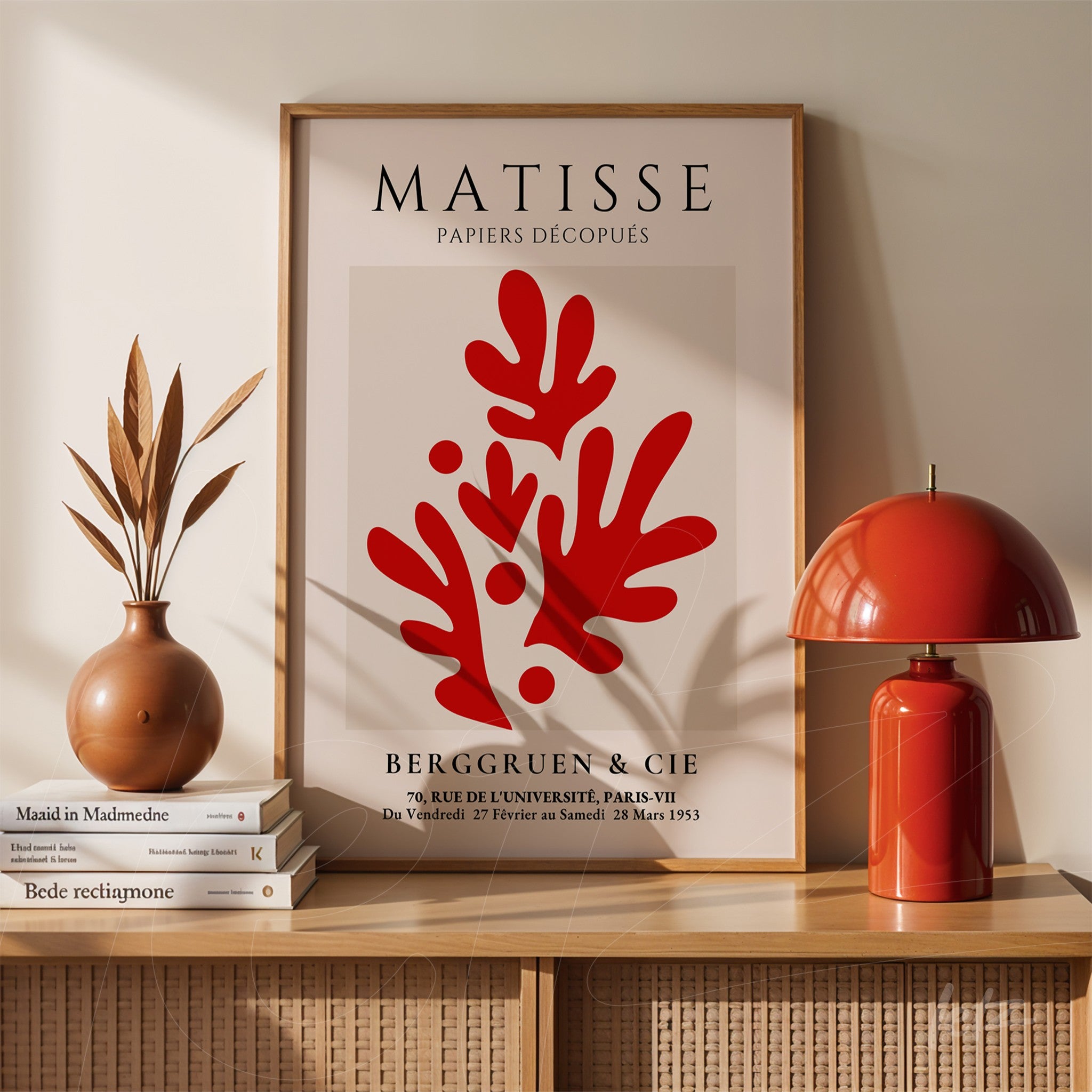 quadro com arte de recortes no estilo de Matisse em moldura de madeira clara, exibido sobre móvel de madeira comudinho e decorado com vaso de cerâmica e luminária vermelha