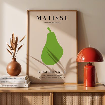 quadro decorativo com arte moderna de uma pêra em verde, moldura simples em madeira clara e fundo bege, exibido sobre uma prateleira com vasos e livros