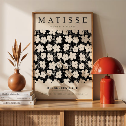 quadro emoldurado com arte de flores e plantas em preto e branco no estilo de Matisse, exibido em uma parede clara com elementos decorativos ao redor