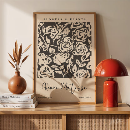 quadro decorativo com estampas de flores em fundo escuro, moldura de madeira clara, apoiado sobre mesa com vaso e abajur