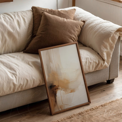 quadro com arte abstrata em tons neutros em moldura de madeira clara, apoiado em sofá com almofadas marrons