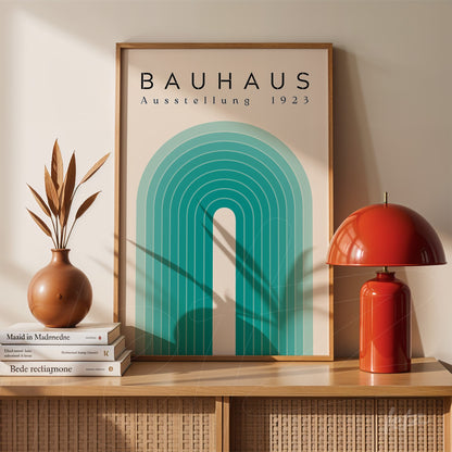 pôster impresso com design geométrico estilo Bauhaus em moldura de madeira clara, exibido sobre móvel de vime ao lado de lâmpada vermelha e vasos decorativos