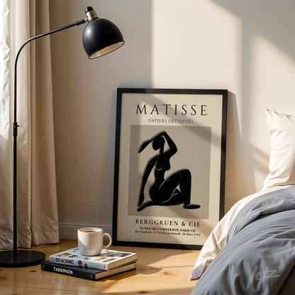 quadro decorativo de arte moderna de figura feminina em moldura preta, apoiado em suporte de madeira ao lado de lâmpada de pé