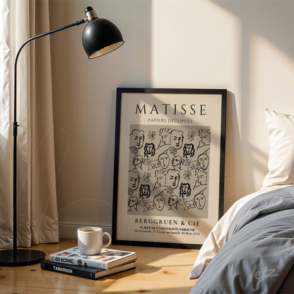 quadro com arte line art em moldura preta com rostos estilizados, apoiado ao lado de uma lâmpada de pé em ambiente bem iluminado