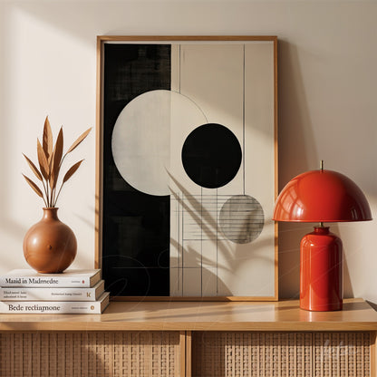 quadro com arte abstrata em preto e branco com formas geométricas em moldura de madeira clara, apoiado em mesa de madeira ao lado de vaso com folhagens secas e luminária vermelha