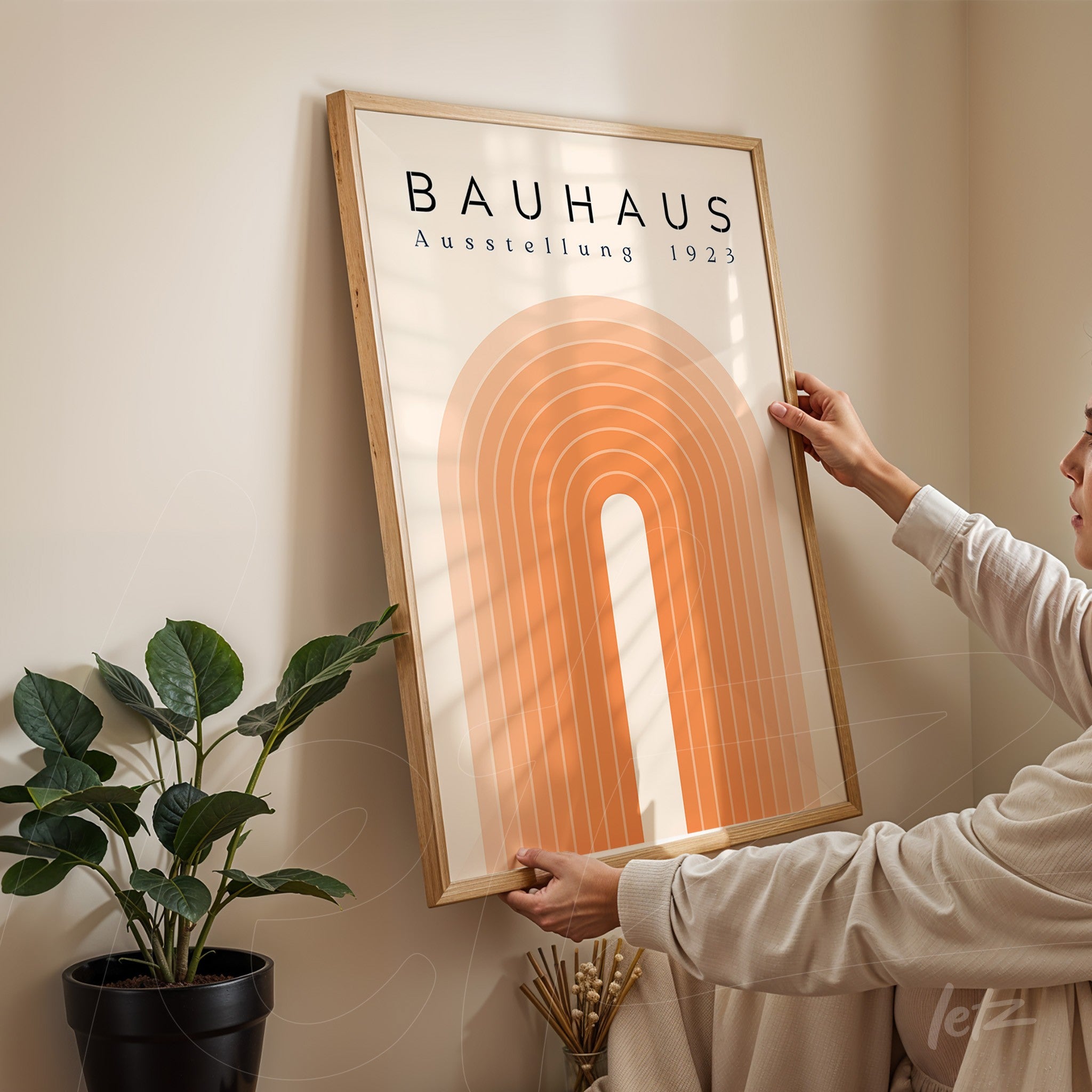 pôster com estilo retrô de arcos concêntricos em tons de laranja, moldura de madeira clara, exibido em parede bege ao lado de planta em vaso