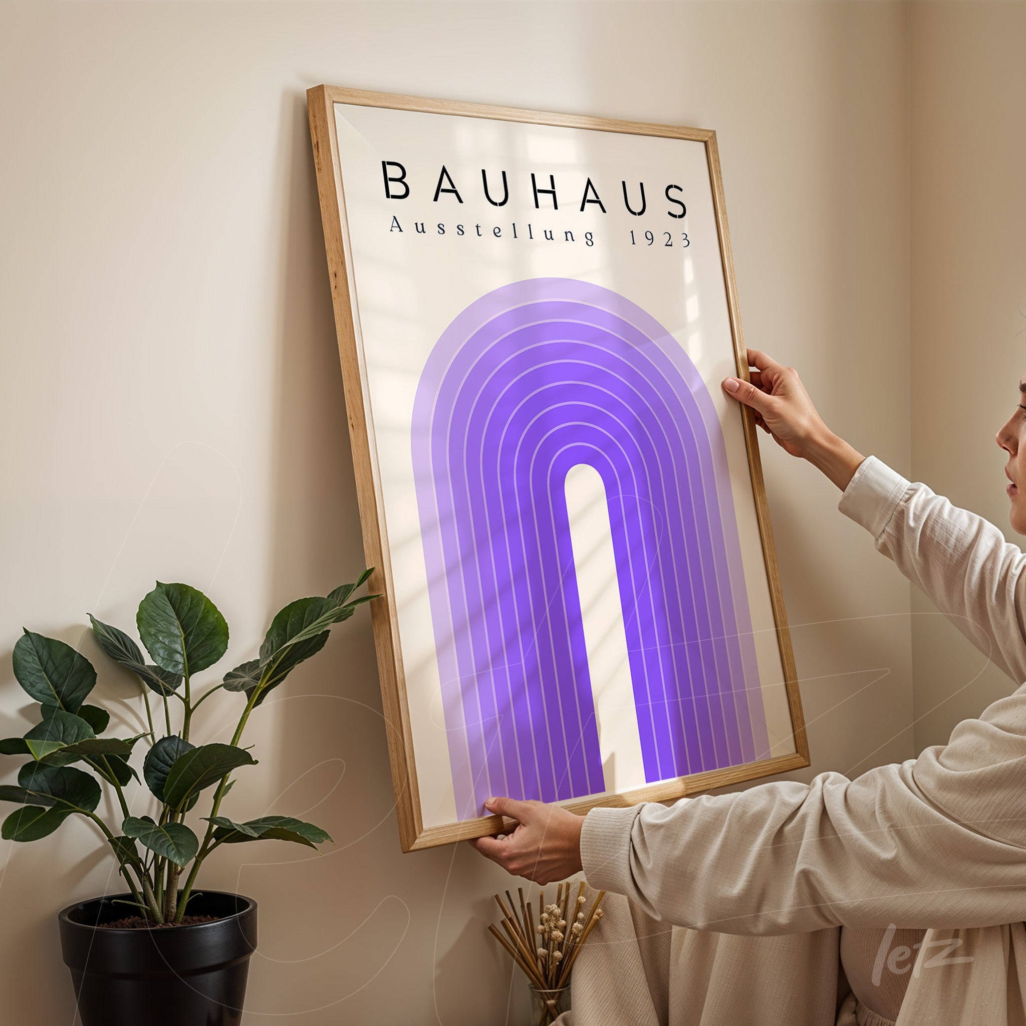 pessoa ajustando quadro de imagem estilo bauhaus com arco roxo e moldura de madeira em parede clara ao lado de planta