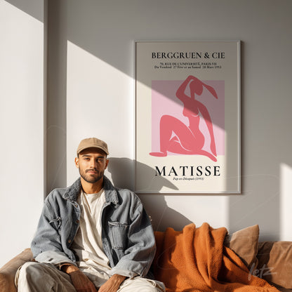 quadro com arte de Matisse em moldura clara, apresentado sobre parede branca com um homem sentado ao lado, vestindo jaqueta de jeans e boné