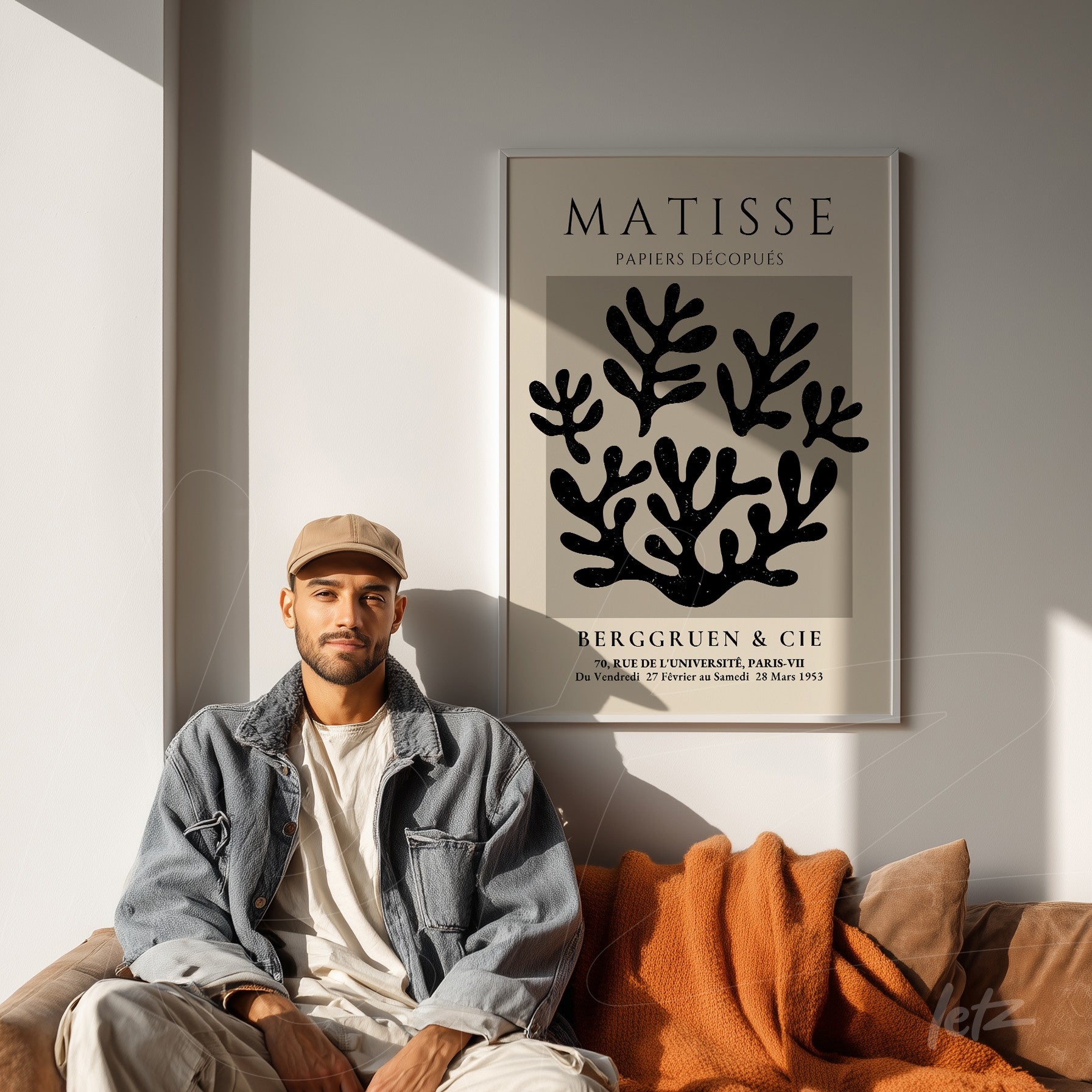 quadro em moldura grande com arte abstrata de folhas pretas em fundo claro, exibido sobre parede clara ao lado de um homem sentado em sofá