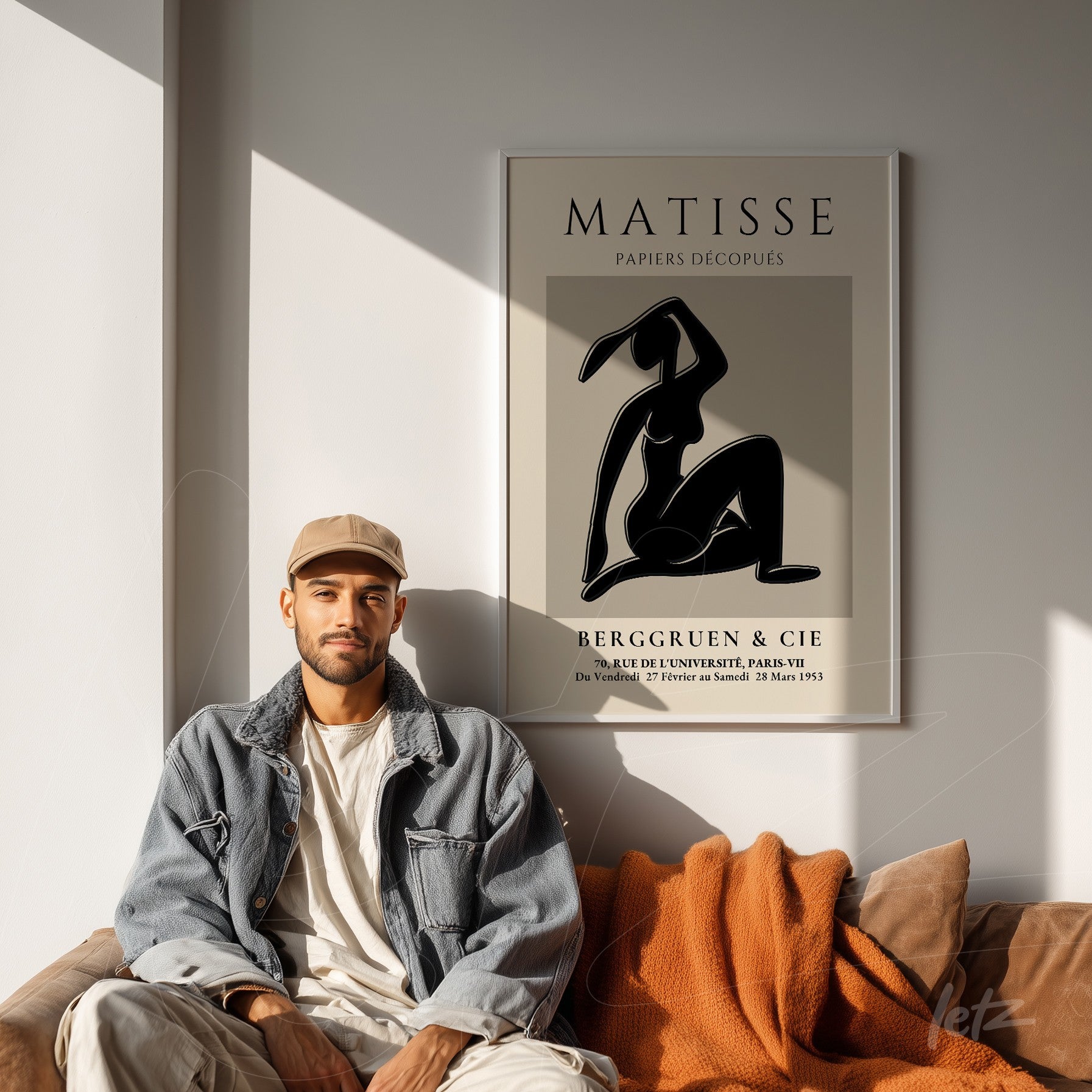 quadro com arte moderna em estilo contorno de figura feminina em moldura clara, exposto em parede clara ao lado de homem com jaqueta de jeans e boné