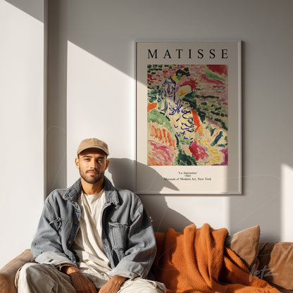 mockup com quadro de arte moderna de Matisse em moldura clara, exibido ao lado de um homem em sofá com almofadas laranja