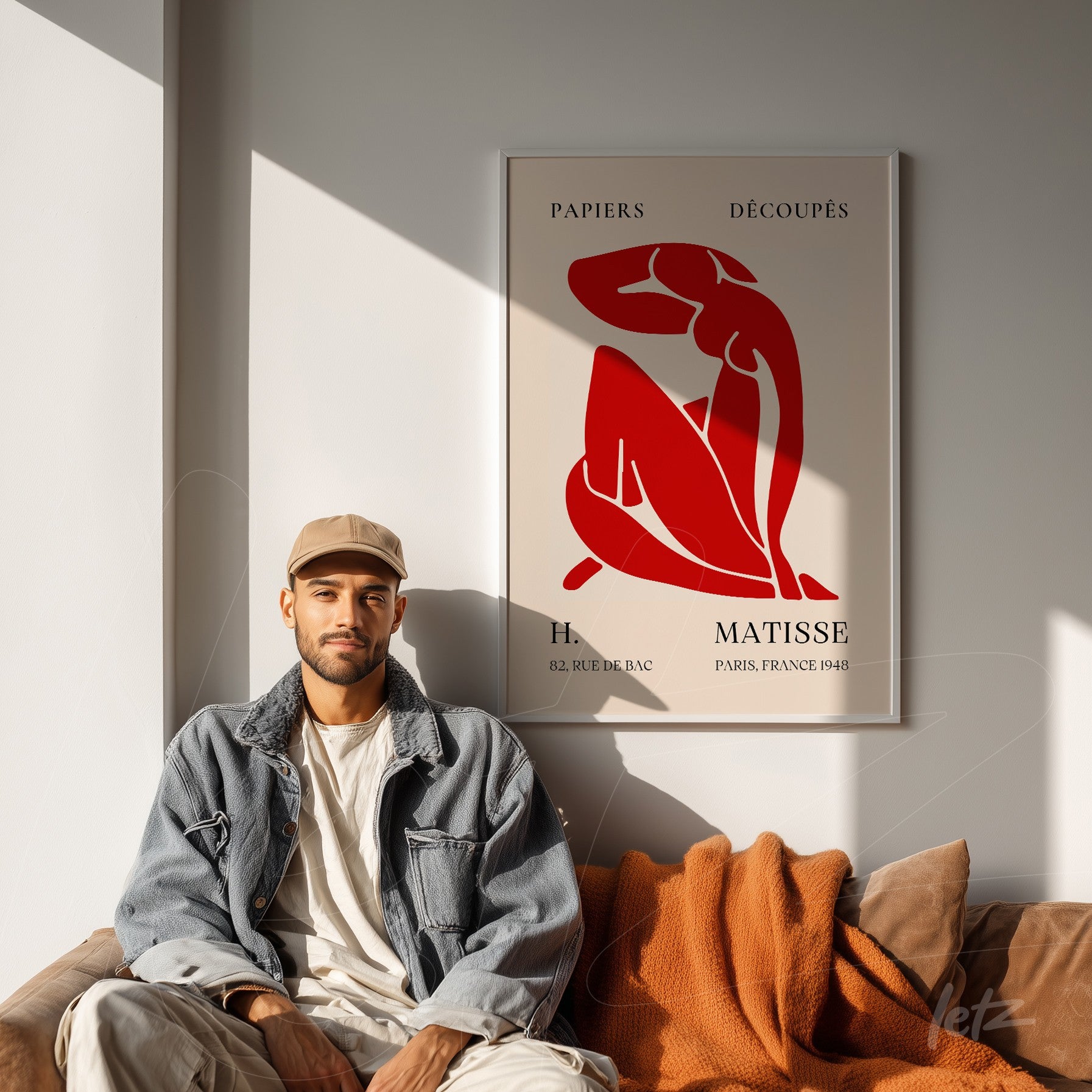 quadro com arte moderna de figura feminina em tons de vermelho e fundo claro em moldura branca, exposto em parede clara ao lado de sofá com cobertor laranja