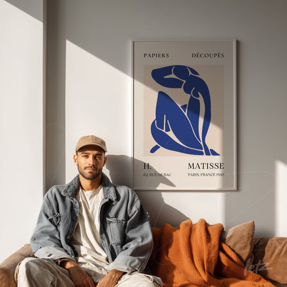 quadro decorativo com arte de Henri Matisse em moldura branca, exibido sobre parede clara com uma pessoa sentada em sofá