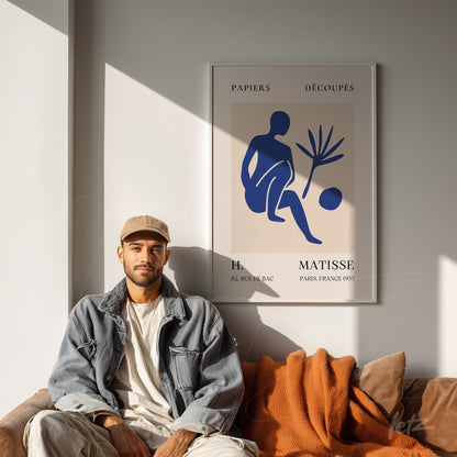 quadro com arte moderna de figura humana em azul sobre fundo claro, moldura branca e em destaque no ambiente com sofá marrom