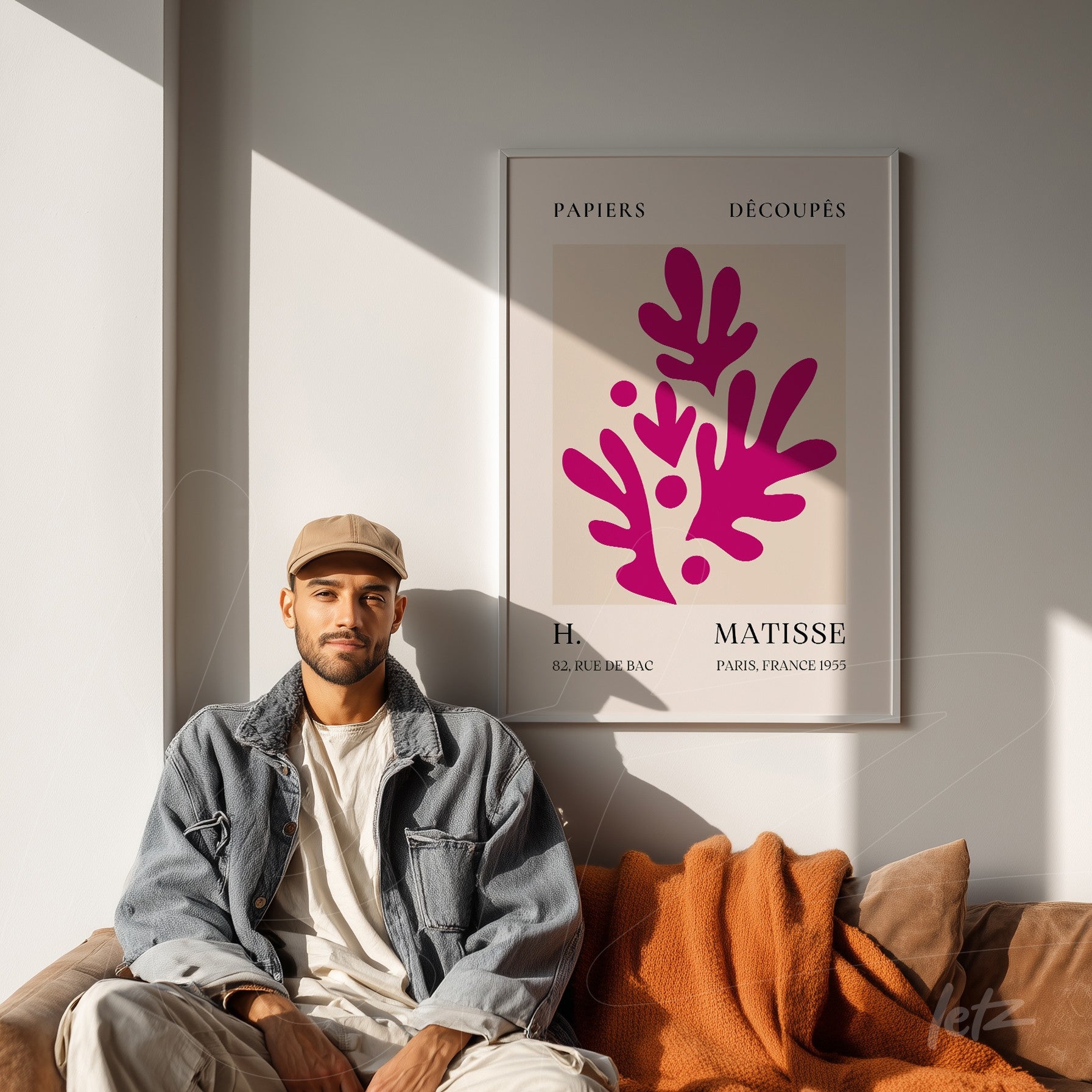 quadro com arte moderna em moldura clara mostrando folhas estilizadas em tons de rosa sobre fundo creme, exibido em parede iluminada com pessoa sentada ao lado