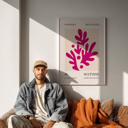 quadro com arte moderna em moldura clara mostrando folhas estilizadas em tons de rosa sobre fundo creme, exibido em parede iluminada com pessoa sentada ao lado